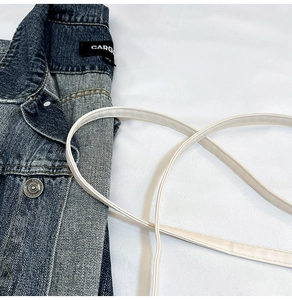 Detail shot of blue denim jacket collar with CARG brand label and white leather strap