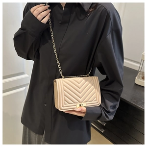 Detail of cream quilted crossbody bag with gold lock and chain strap on a black shirt