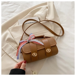 Detail of woven cylinder handbag with metal locks and tricolor ribbon on white fabric