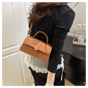 Detail of a brown leather handbag with minimalist stitching and adjustable strap
