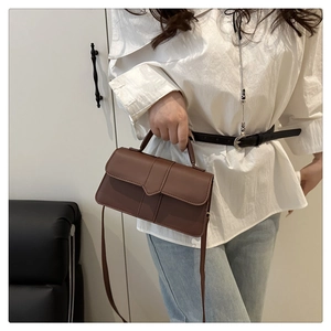 Sac à main en cuir marron foncé mat porté avec une chemise blanche et un jean bleu