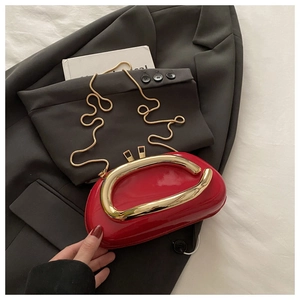 Détail du sac en cuir verni rouge avec boucle fer à cheval dorée sur un blazer gris