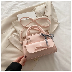 Detail of light pink shell bag featuring a delicate bow and black-white plaid ribbon