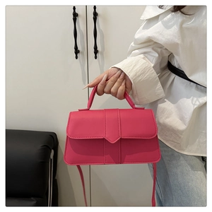 Détail du sac bandoulière rose avec poignée et garniture verticale porté à la main