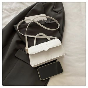 Detailed view of white leather handbag with adjustable strap on a gray blazer