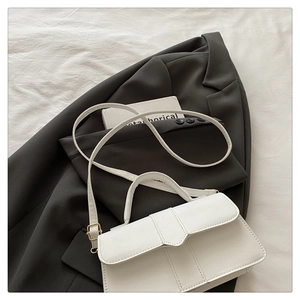 Detail of white leather handbag with V-shaped flap and vertical stitching on black blazer