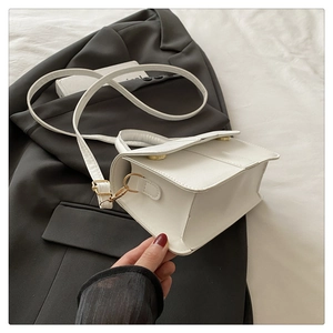 Detail view of white minimalist square handbag with gold hardware and accordion side pleats