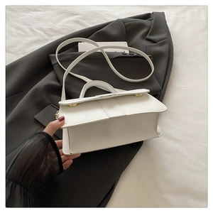 Detailed view of a white leather rectangular handbag with gold hardware on a dark blazer
