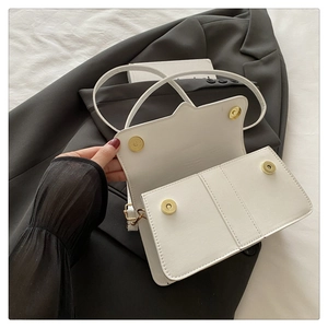 Detail view of white leather handbag featuring wavy flap design and gold magnetic buckles