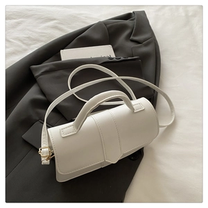 Detail shot of a white minimalist handbag on a gray blazer with handle and strap