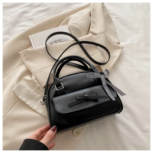 Detail of black shell bag featuring a bow pocket, silver hardware and a plaid ribbon scarf