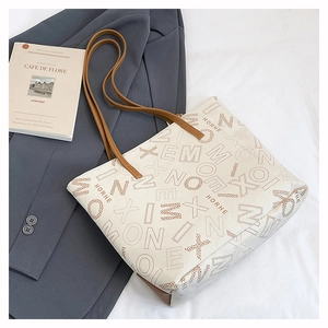 Detail of cream tote bag with brown letter patterns on grey blazer and book