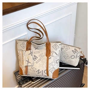 Three-piece tote bag set with letters and brown trim shown on a metal suitcase