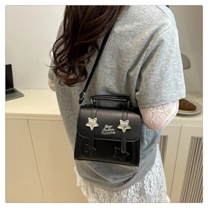 Detail of black crossbody bag with silver stars and adjustable shoulder strap worn by model