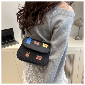 Détail du petit sac bandoulière noir avec autocollants colorés porté par un mannequin