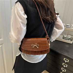Borsa a tracolla marrone motivo coccodrillo con fiocco dorato indossata da una modella
