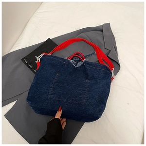 Detail of blue denim tote bag with red strap and raw fringe edges in V-shape design