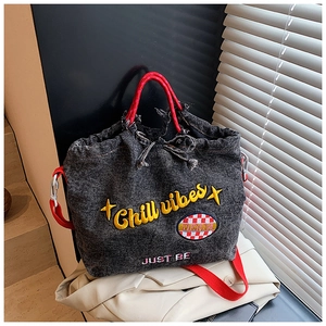 Detail of grey denim crossbody bag with Chill Vibes embroidery and red strap