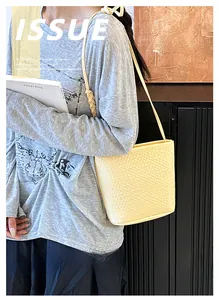 Detail of light yellow woven crossbody bucket bag with slender shoulder strap texture