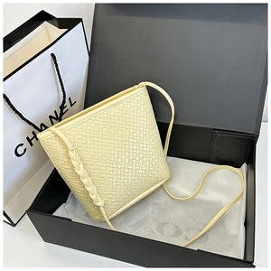 Detail of light yellow woven bucket bag with intricate braided strap in a luxury gift box