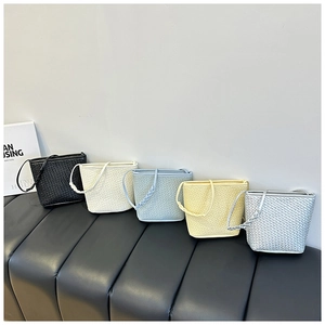 Collection of five woven bucket bags in various colors displayed on a leather bench
