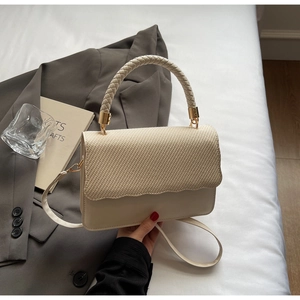 Gros plan détaillé d'un sac bandoulière tressé crème avec rabat texturé et métal doré