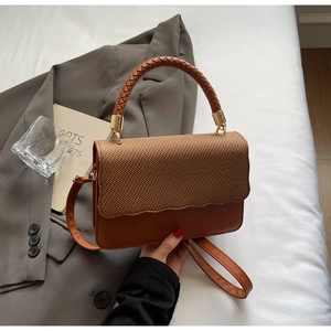 Détail d'un sac bandoulière en cuir marron avec rabat tissé et poignée tressée chic
