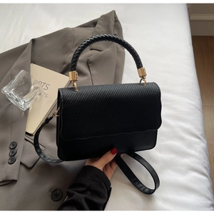Détail du sac à bandoulière noir montrant le rabat texturé et la poignée tressée chic