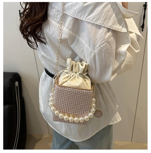Detail of woven bucket bag with pearl handle and golden chain strap on a model