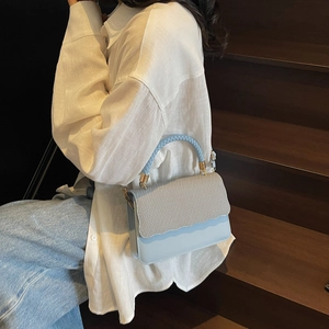 Light blue crossbody bag with woven texture handle and wavy flap design on white shirt