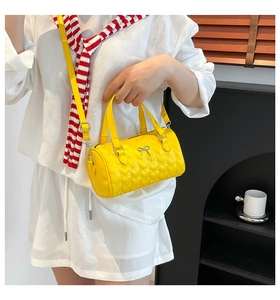 Detalle del bolso cilíndrico amarillo con patrón de corazones acolchados y lazo metálico