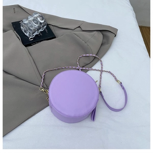 Detail of a purple round crossbody bag with metal chain strap on a white sheet backdrop