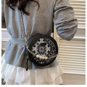Detail of round crossbody bag featuring ethnic embroidery and decorative white pearls