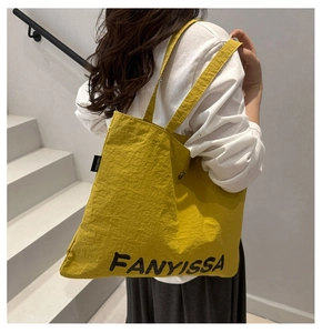 Large yellow canvas tote bag with black letter print worn by model on shoulder