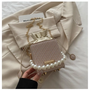 Detailansicht der beigen Jacquard-Beuteltasche mit Perlengriff und goldener Kettenriemen