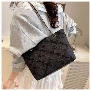 Close-up of black quilted shoulder bag with chain strap worn by a model in soft lighting