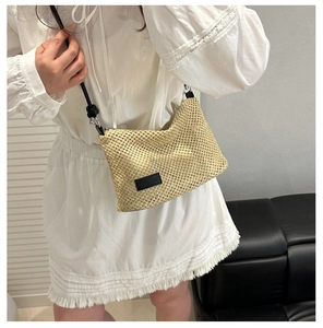 Detail of a beige woven crossbody bag featuring a black logo patch and slim leather strap