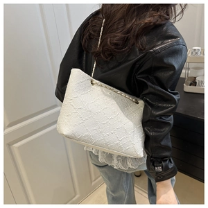Detail of white woven tote bag with metallic chain strap worn on shoulder with leather jacket