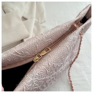 Close-up of pink embroidered handbag featuring gold zipper closure and chain strap details