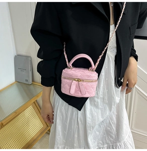 Detail of pink quilted square bag with gold chain strap and top handle worn by model