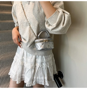 Silver quilted mini crossbody bag with gold chain strap shown on a model in a casual outfit