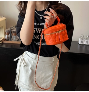 Close-up of orange quilted crossbody bag with dual gold zippers and chain strap