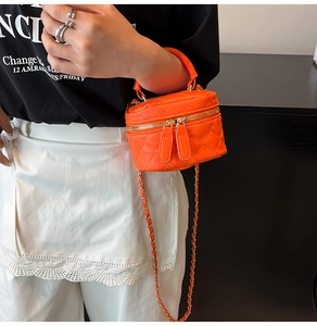 Detail of bright orange quilted PU leather mini bag with gold chain strap on model