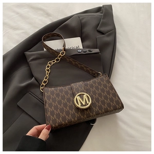 Detail of dark brown leather underarm bag with M-letter pattern and golden metal buckle