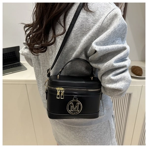 Vue détaillée d'un sac boîte noir avec emblème M doré et bandoulière réglable