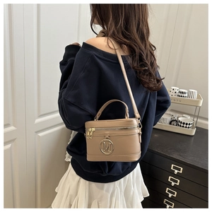 Detail of beige crossbody bag with gold M logo and adjustable strap on female model