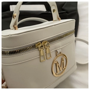 Dettaglio della borsa in pelle bianca con doppia cerniera dorata e logo M in metallo