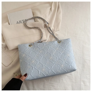 Close-up of light blue quilted tote with floral embroidery and gold chain strap details