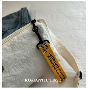 Détail du sac cylindrique en nylon crème avec ruban jaune et crochet en métal noir mat