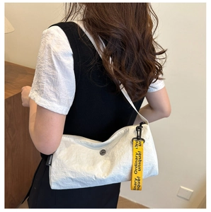 Detailansicht der weißen Nylon-Schultertasche mit gelbem Zierband am Modell getragen